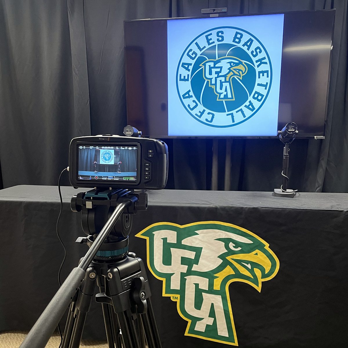 Camera on a tripod, monitor and microphone set up in front of a CFCA-branded interview table and display.